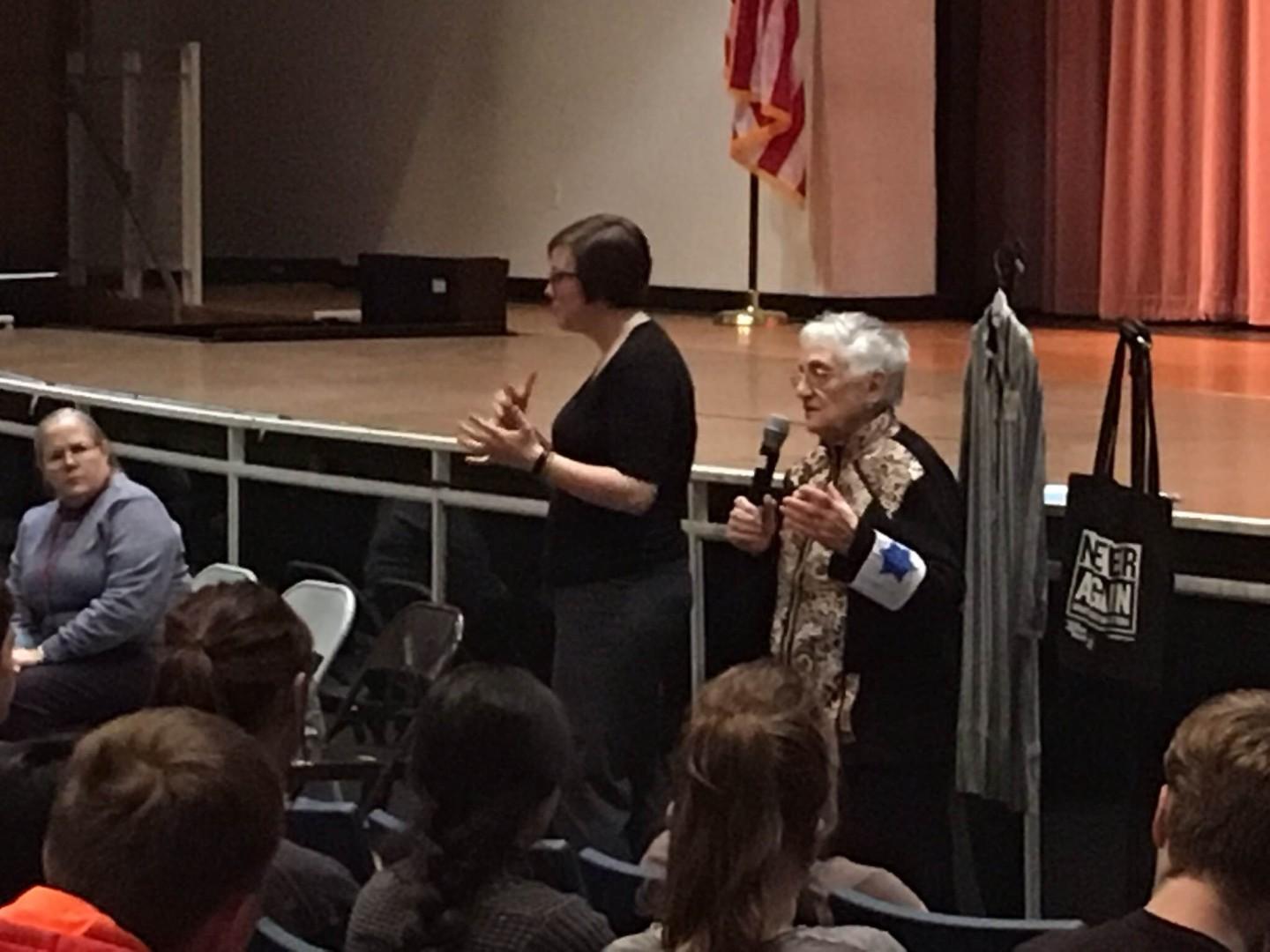 Holocaust survivor Edith Lowy (right) speaks to RHS students Feb. 23. She is wearing a replica of the Star of David armband she was forced to wear in the Wieliczka ghetto. To her right are a replica of a concentration camp prisoner's outfit and a tote bag from the United States Holocaust Memorial Museum that reads